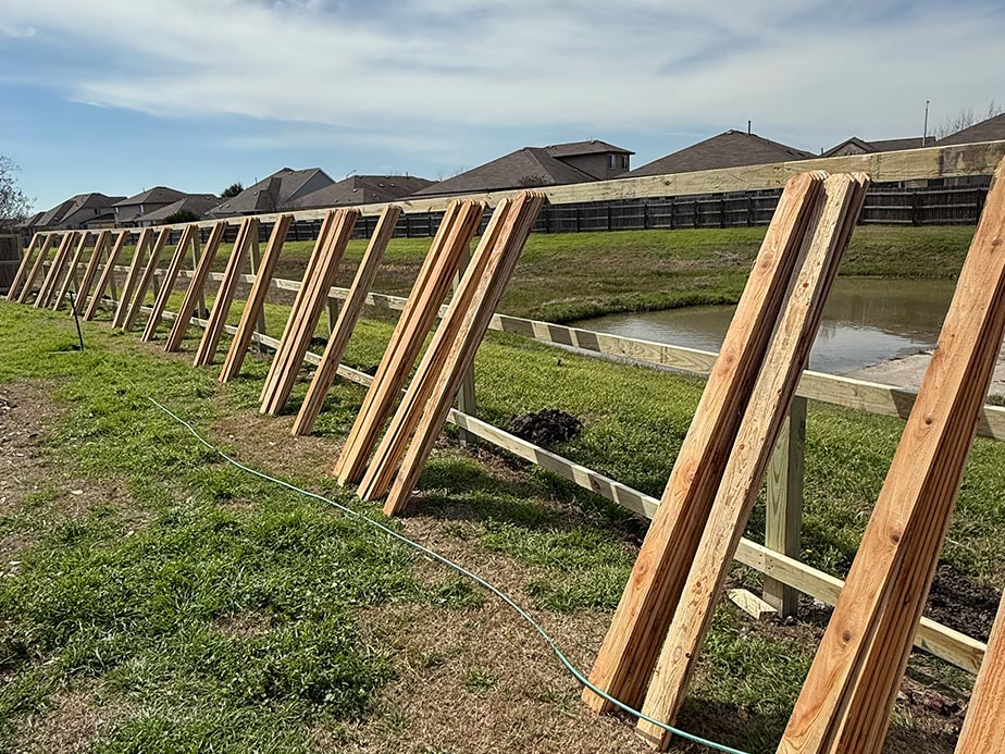 Partially built wooden fence with vertical planks and horizontal rails near residential homes